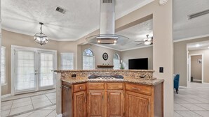 A spacious kitchen with a granite countertop, wooden cabinets, and a central island. - Amazing Bay Villa Near NASA with Pool & Pool Table (Houston)