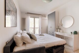 Un dormitorio con cama, mesita de noche, cómoda, espejo y ventana.