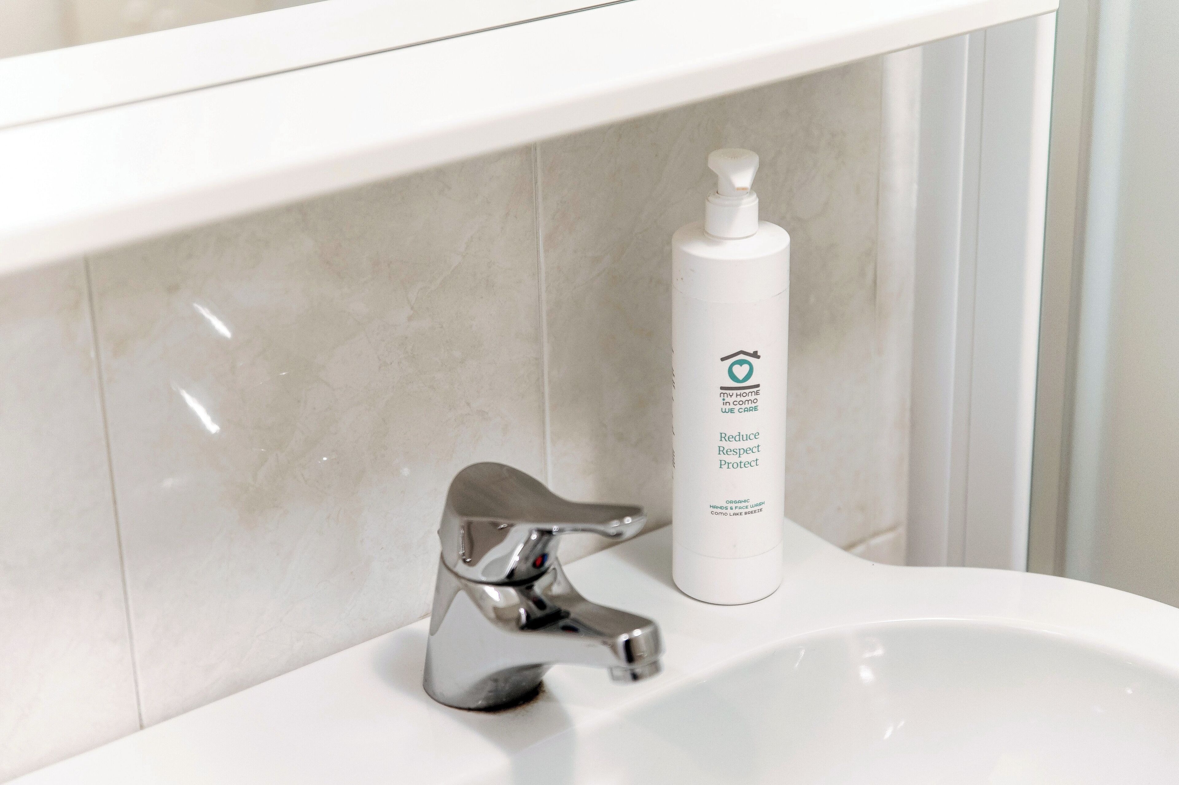 A bathroom sink with a chrome faucet and a white bottle of liquid soap.