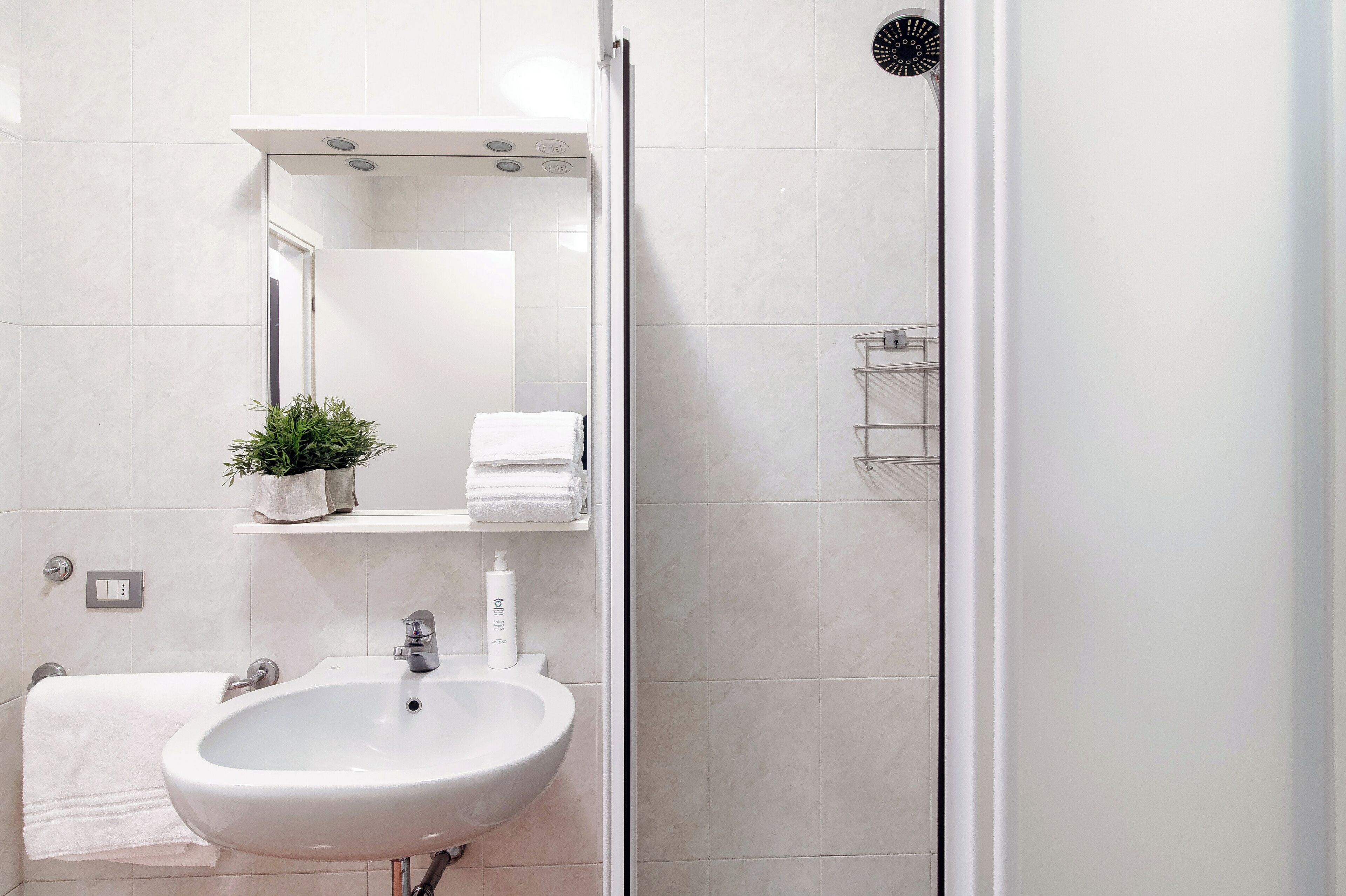 Une salle de bain moderne avec un lavabo blanc, un miroir, un porte-serviettes et un espace douche.