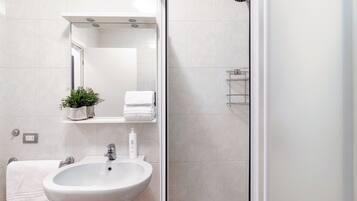 Une salle de bain moderne avec un lavabo blanc, un miroir, un porte-serviettes et un espace douche.