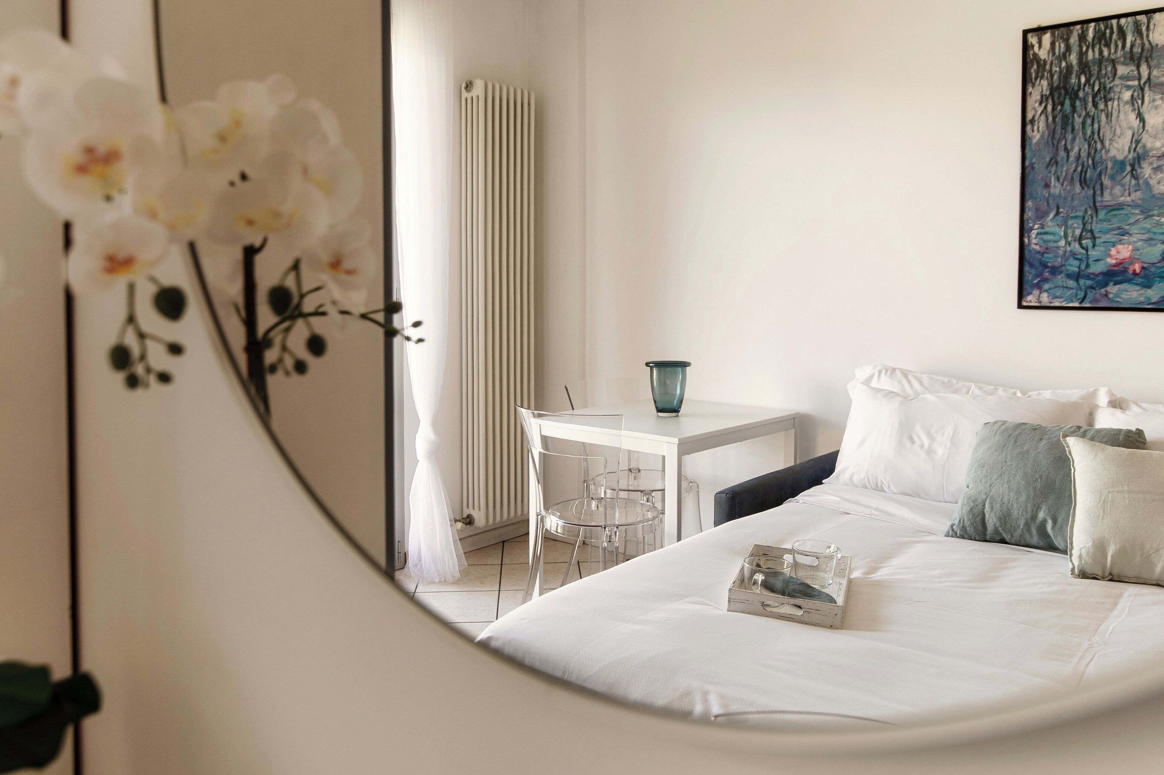 A bedroom with a bed, a desk, and a chair. There is a radiator and a painting on the wall.