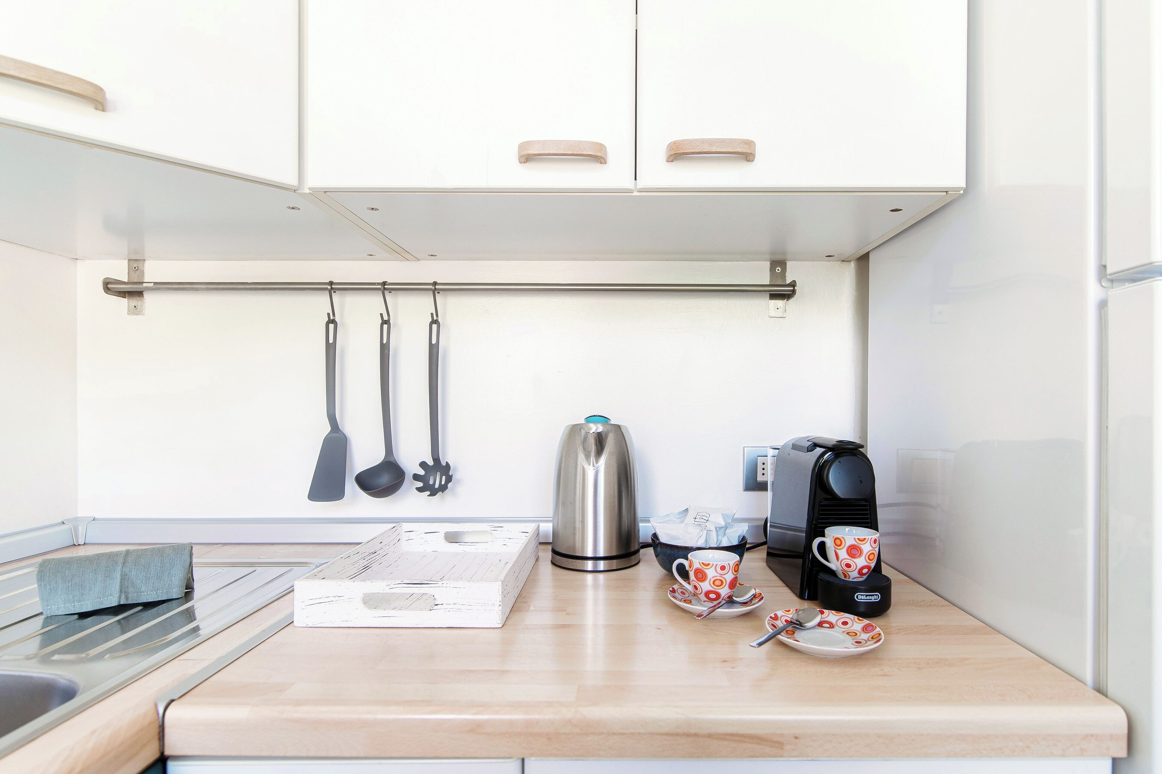 A compact kitchen with a stainless steel kettle, a coffee maker, and a kettle hook on the wall.