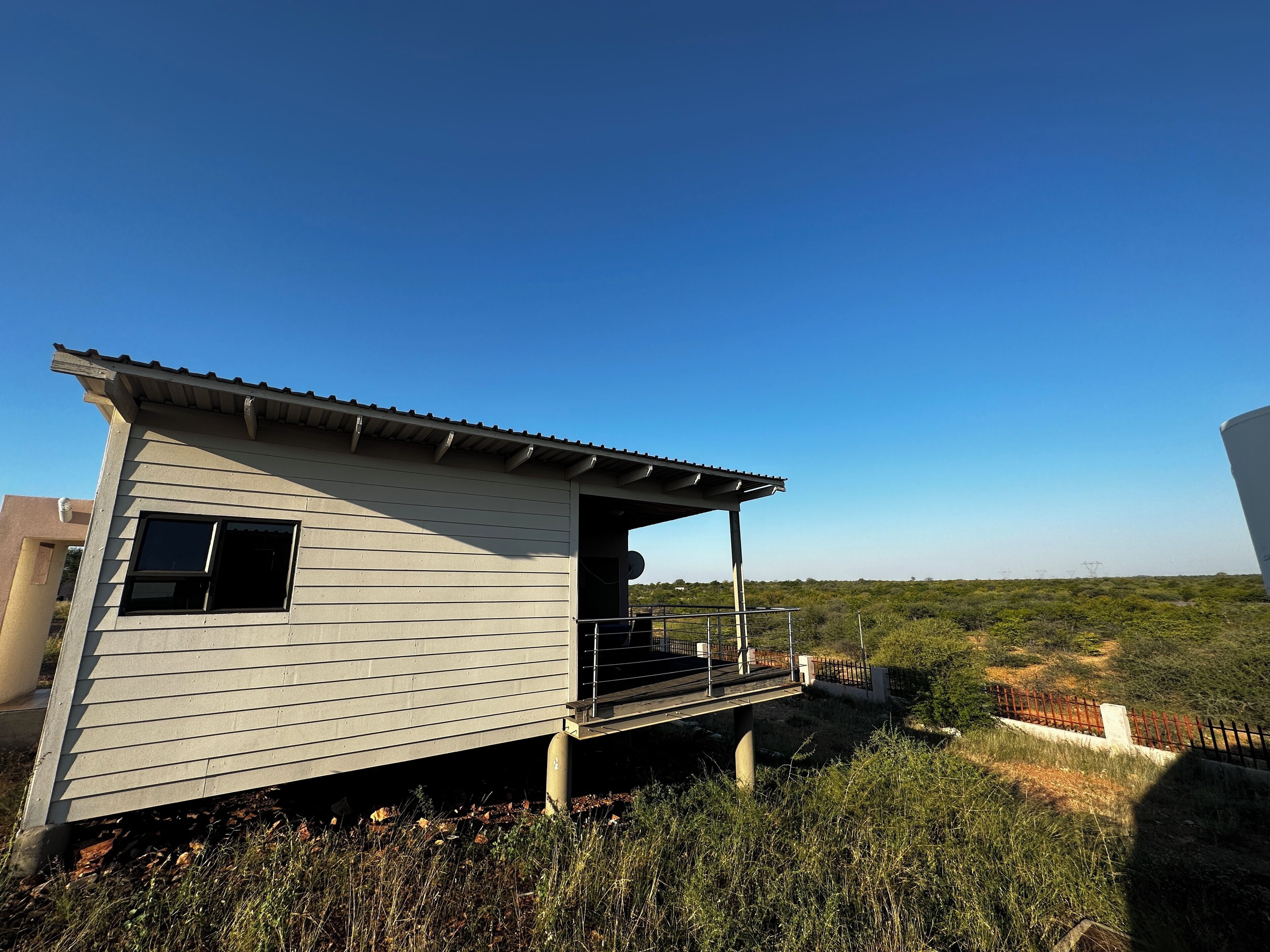 A single-story building with a balcony, situated in a grassy area with a clear sky.