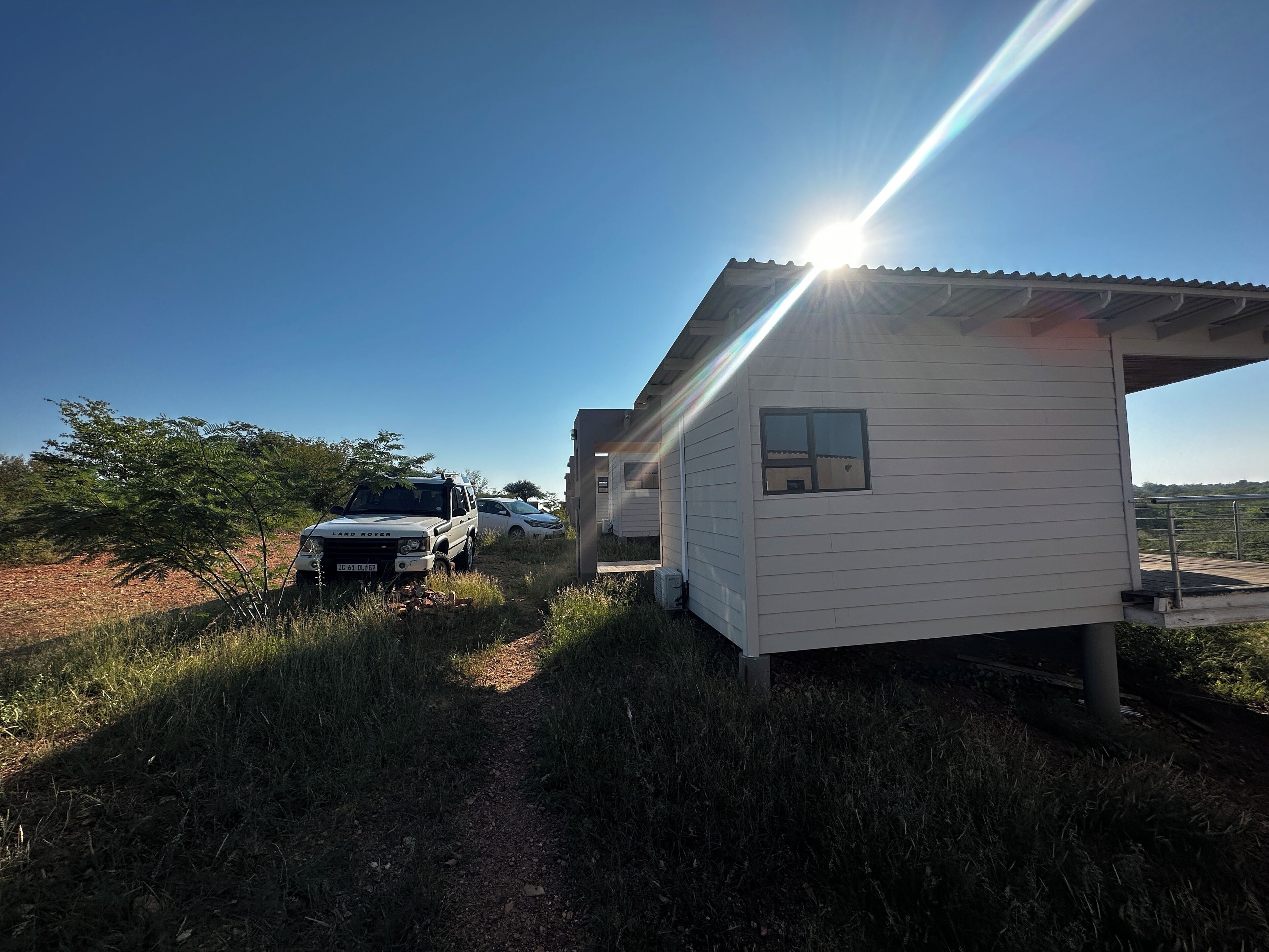 A small white building with a metal roof, a paved pathway leading to it, and a parked Land Rover.