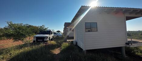A small white building with a metal roof, a paved pathway leading to it, and a parked Land Rover.