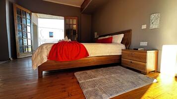 A bedroom with a wooden bed, a nightstand, a bedside table, a rug, and a view of the outside.
