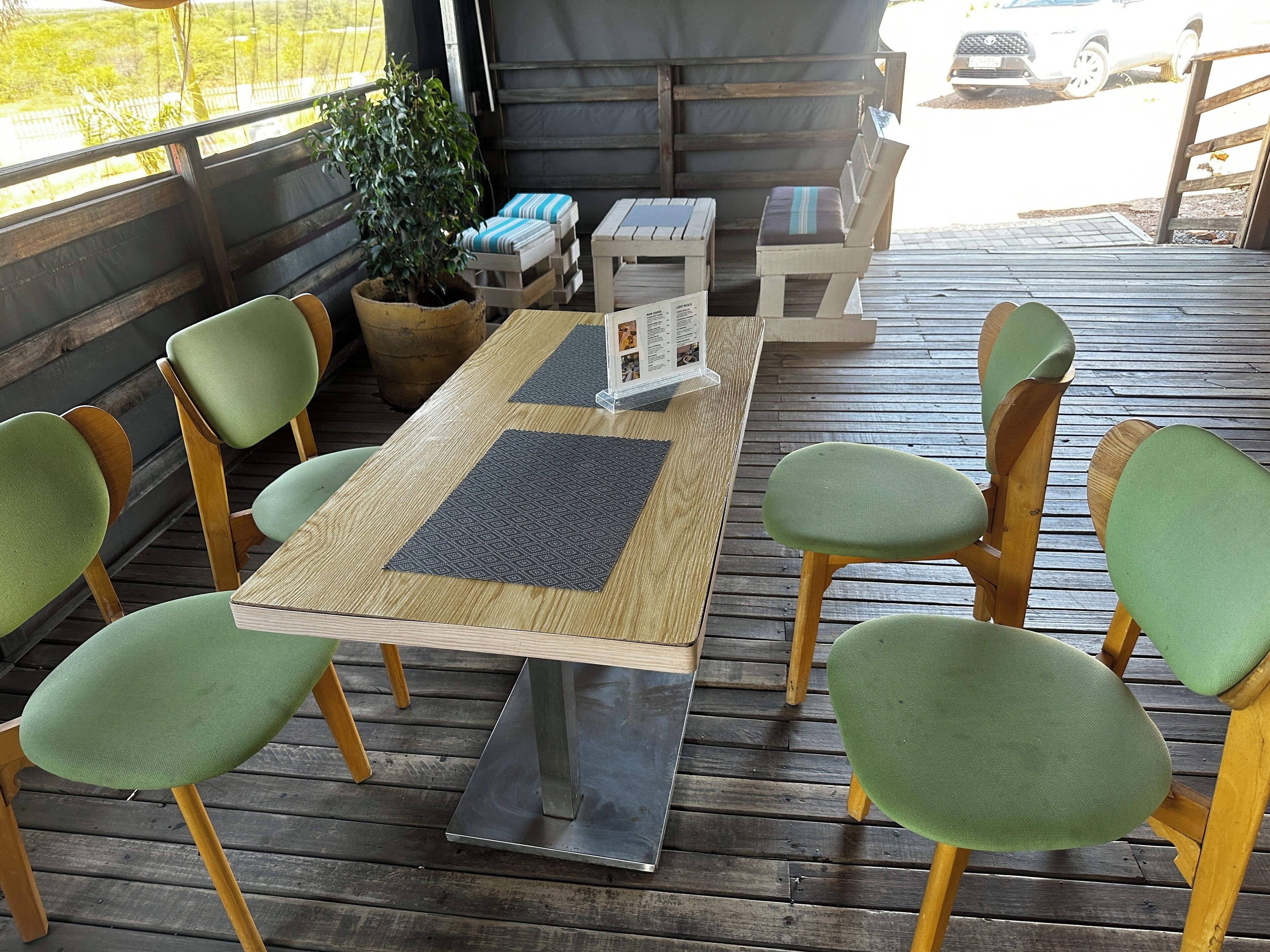 A wooden deck with a table and chairs, a potted plant, and a menu stand.