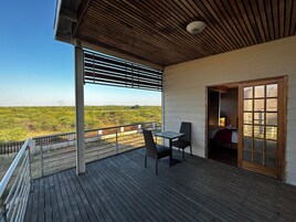 Una terraza de madera con mesa y sillas, vista al campo y una puerta que da a un espacio interior.