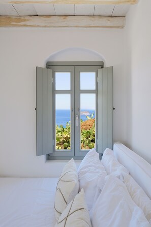 A bedroom with a large window overlooking a coastal landscape. - Odyssey Rock (Milos)