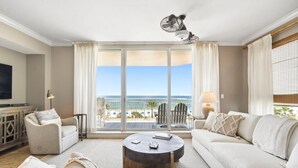 A spacious living room with a large window overlooking the beach, a ceiling fan, and a cozy seating area with a coffee table. - Indigo East 406 (Pensacola)