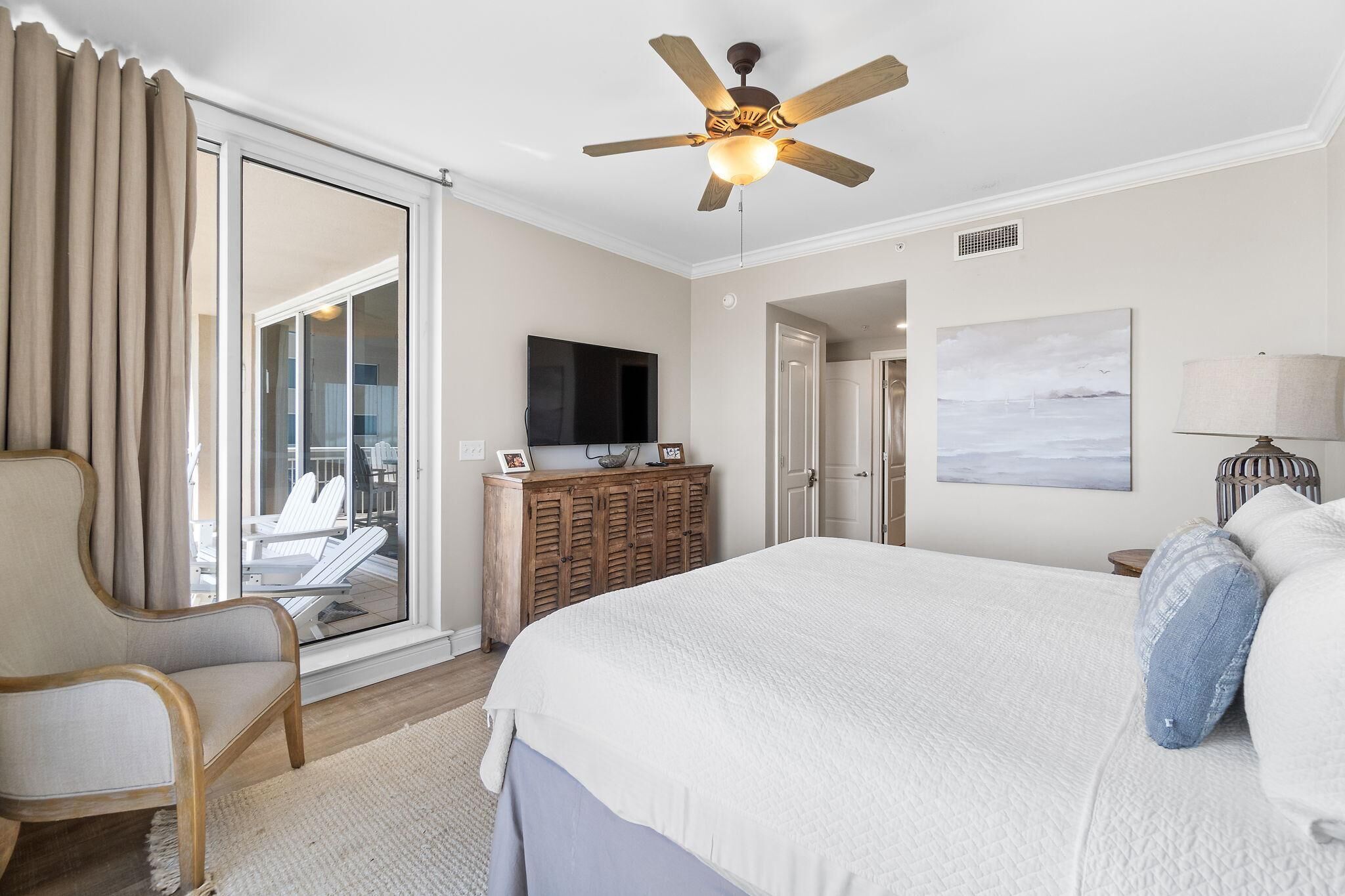 A bedroom with a bed, a chair, a television, a cabinet, and a ceiling fan.