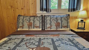Ein Bett mit einer Bettdecke mit Wald- und Reh-Muster, einem hölzernen Kopfteil und einem Nachttisch mit Lampe.