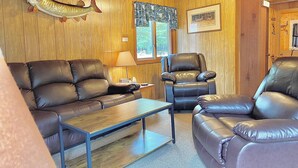 Ein gemütliches Zimmer mit Holzwänden, einem großen an der Wand befestigten Fisch, einem Ledersofa, einem Ledersessel und einem kleinen Tisch.