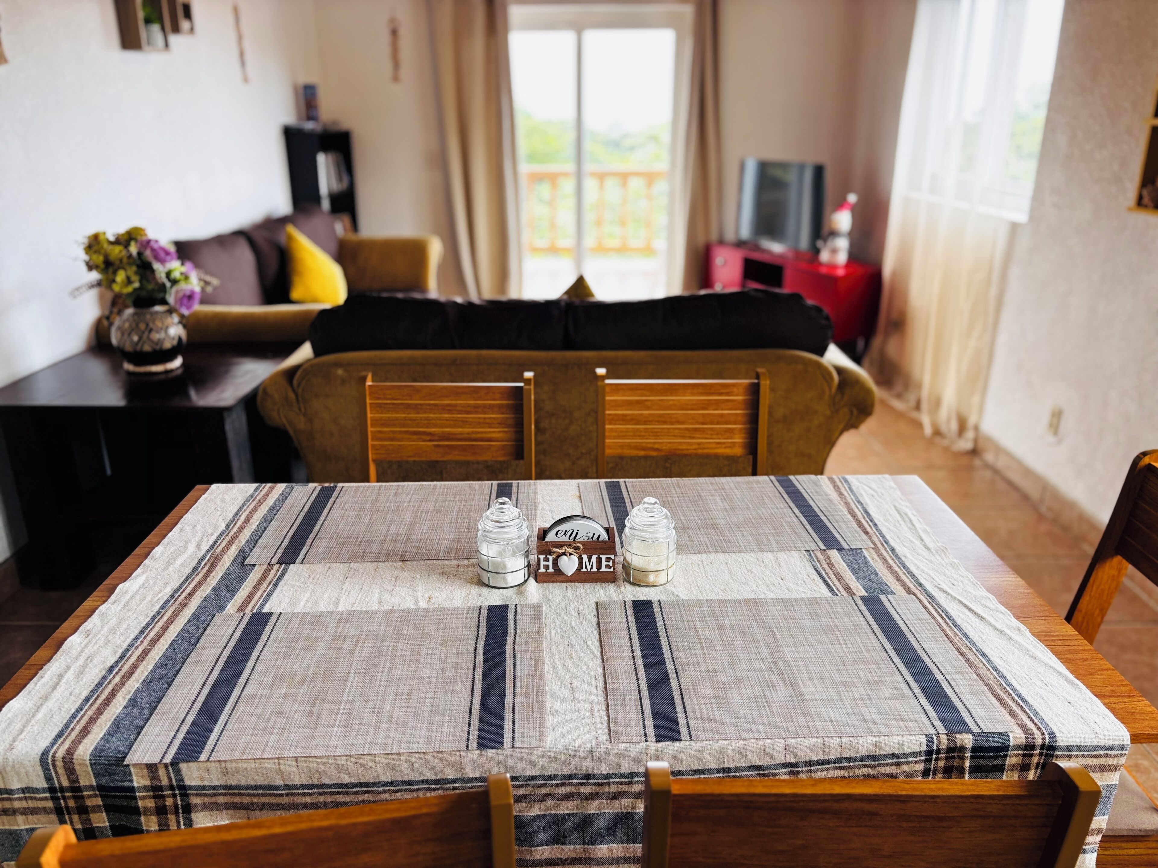 Une table à manger recouverte d’une nappe à carreaux, avec deux salières et deux poivrières, et un panneau sur lequel on peut lire le mot « MAISON ».