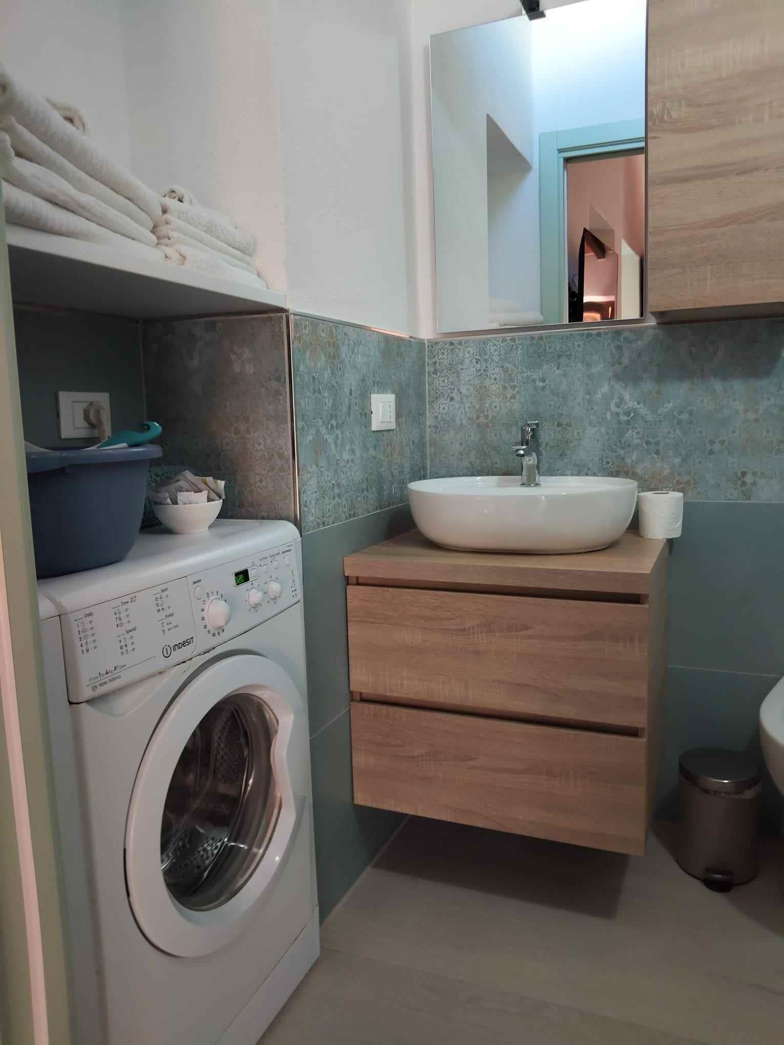 Un espace buanderie compact comprenant un lave-linge, un évier et un miroir.
