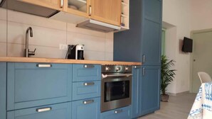Une cuisine avec des meubles de couleur bleue, un four en acier inoxydable et une machine à café posée sur le plan de travail.