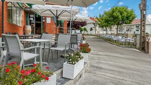 Ein Straßencafé mit Tischen und Stühlen vor einem Backsteinhaus, eine Reihe geparkter Autos.