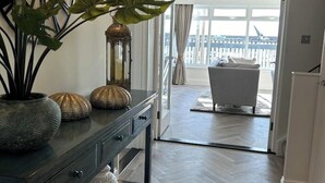 A modern interior with a dark wooden console table, decorative vases, and a potted plant. A view of a balcony with a white railing and a bathtub is visible through an open door. - Ultimate Gorey Retreat (jersey)