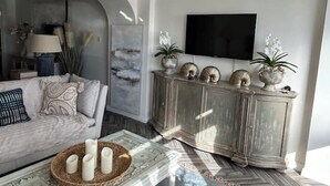 A living room with a sofa, a coffee table with candles, a TV mounted on the wall, and decorative items on a cabinet. - Ultimate Gorey Retreat (jersey)