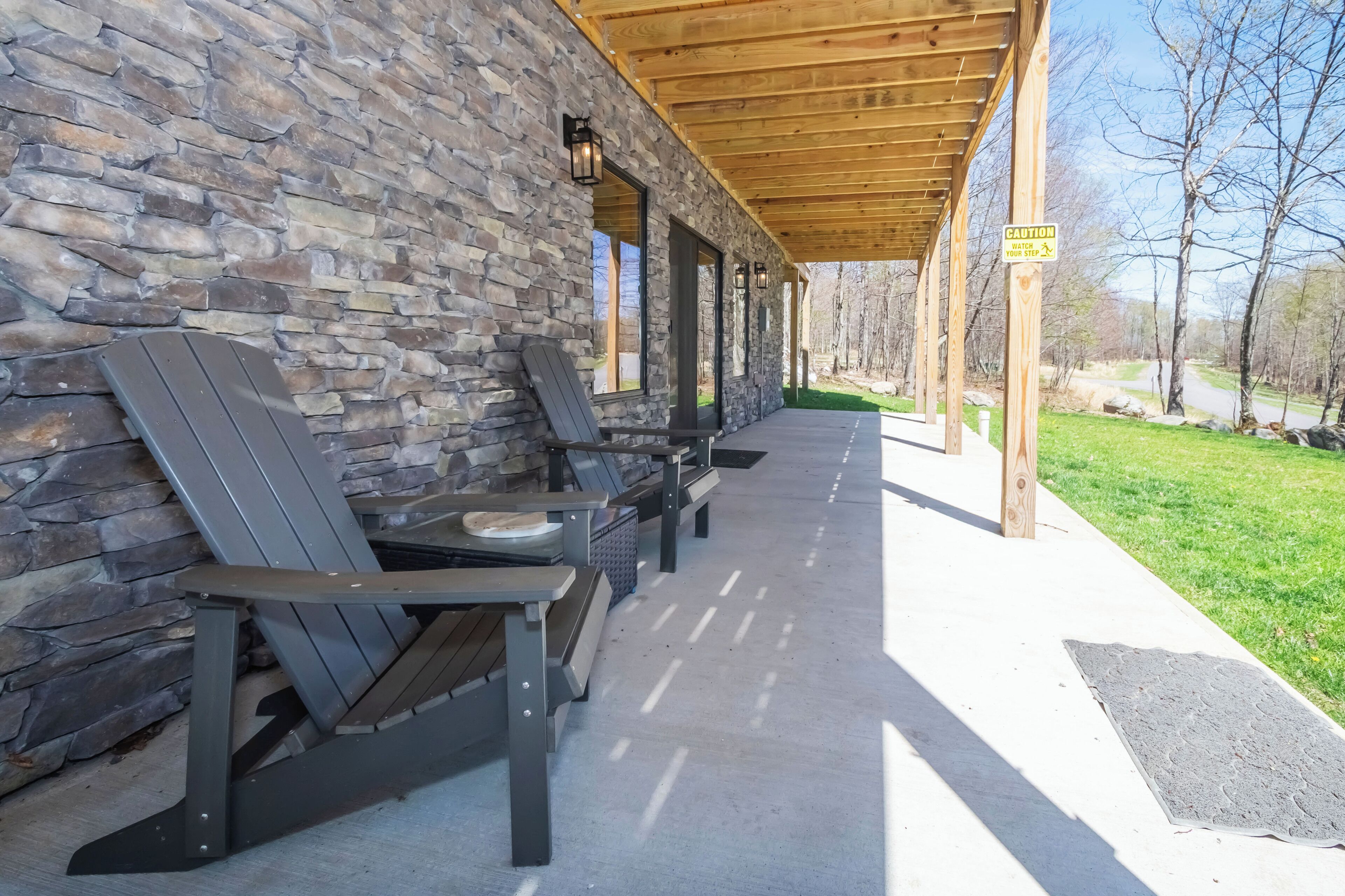 Een overdekt terras met Adirondack-stoelen en een stenen muur.