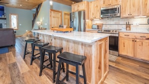 Een keuken met houten kastjes, een roestvrijstalen koelkast, een magnetron en een groot eiland met barkrukken.