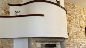 Una sala de estar acogedora con una chimenea de piedra, un repisa blanca y adornos como un jarrón con plantas secas y pequeñas casas de madera.