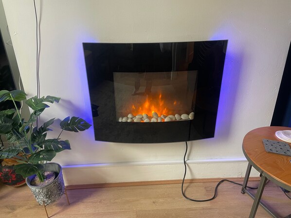 Een moderne haard met een glazen voorpaneel, een potplant aan de linkerkant en een tafel met een onderzetter aan de rechterkant.