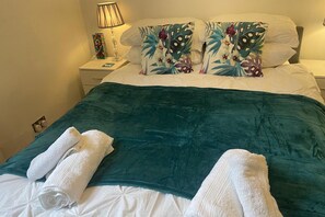 A neatly made bed with a teal bedspread, white pillows, and two white towels. - 1 Bed Victorian Flat Sleeps 4 - Garden & Patio (London)