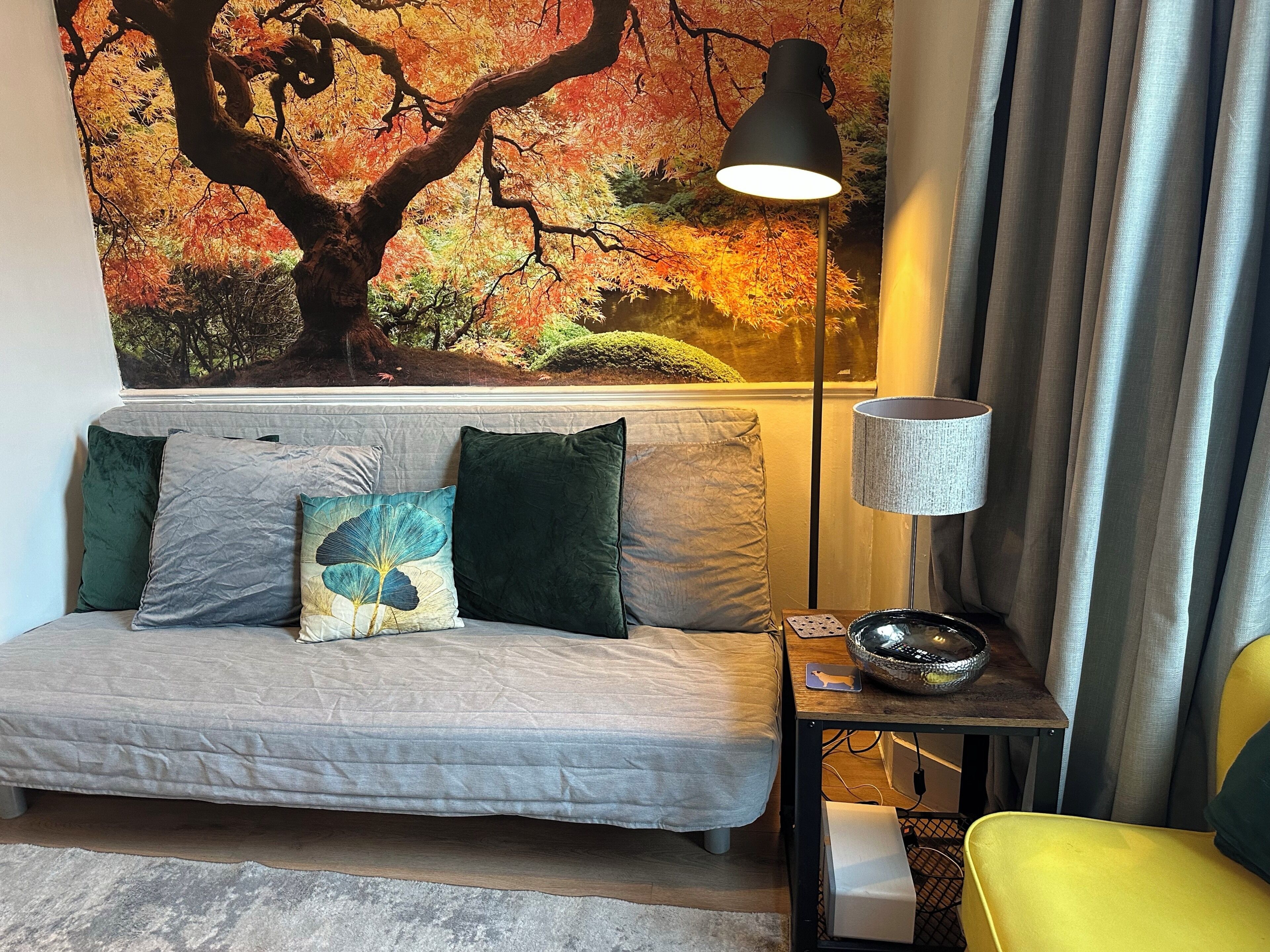 A living room with a sofa, pillows, a lamp, and a decorative wall.
