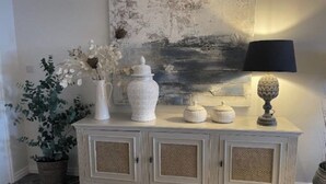 Un meuble blanc à trois portes, un vase avec des fleurs et une lampe sur le dessus.