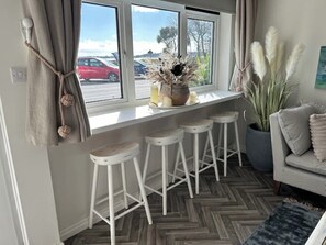 A kitchen area with a window overlooking a parking lot, a white countertop with stools, and a potted plant. - Gorey Retreat Ground Floor (jersey)