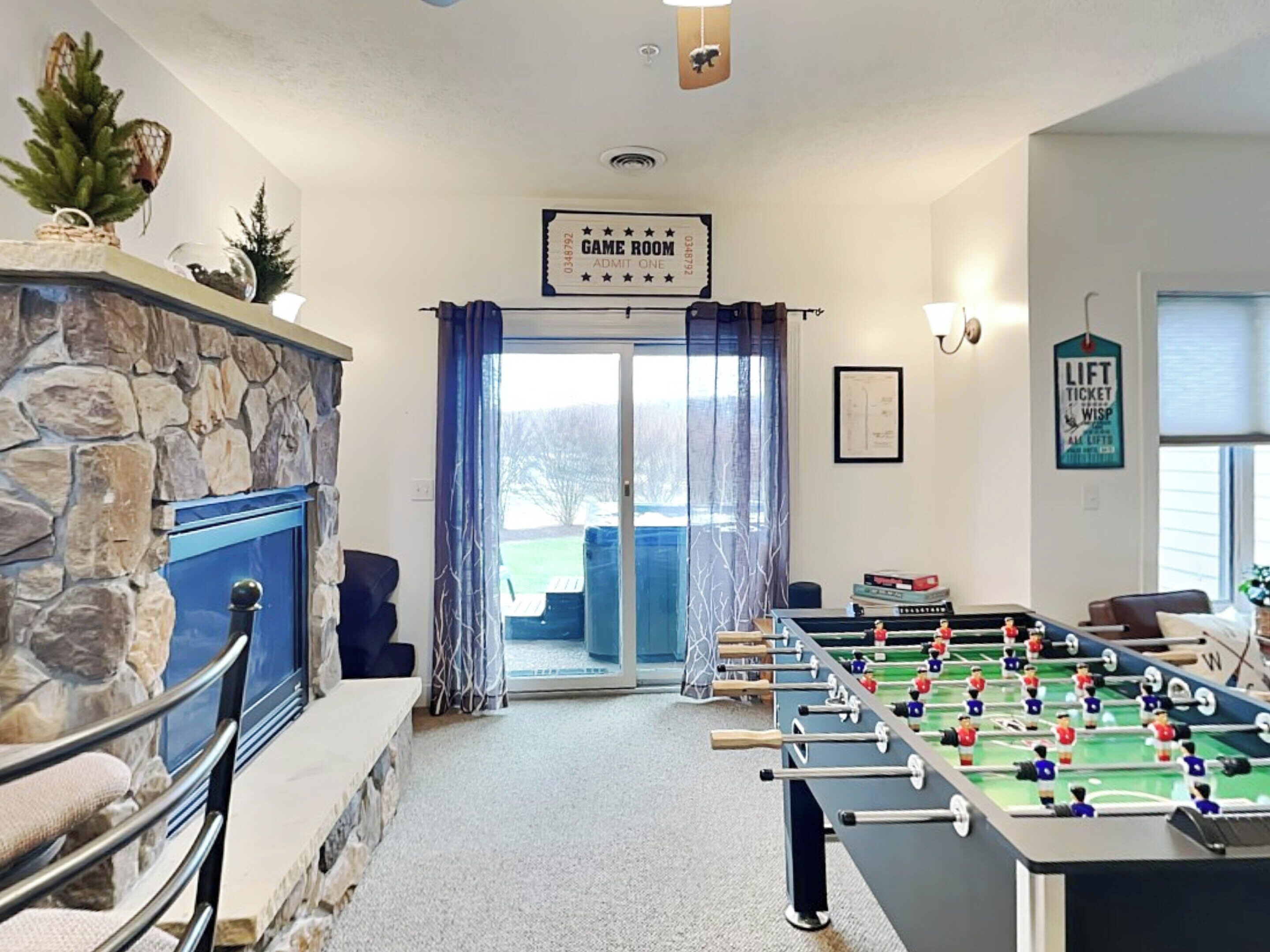 A room with a foosball table, a stone fireplace, and a sign that reads "GAME ROOM ADMIT ONE".