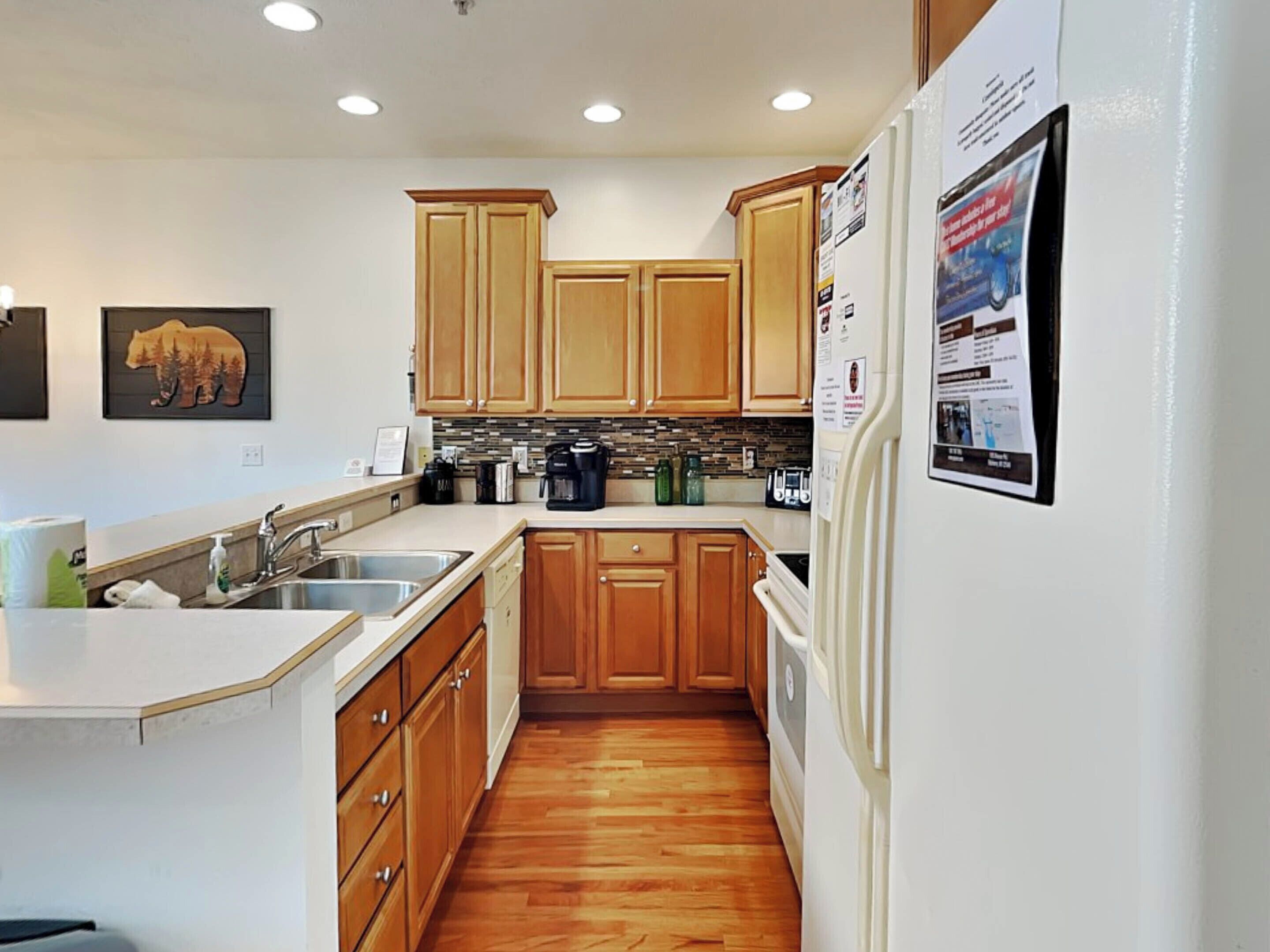 Una cocina con armarios de madera, un refrigerador, una cafetera y un adorno de pared con temática de osos.