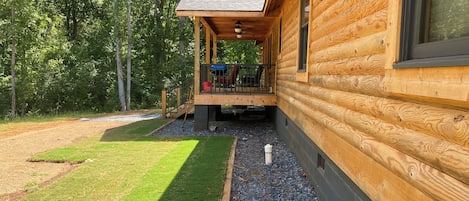 A wooden cabin with a covered porch, a gravel pathway, and a grassy yard.