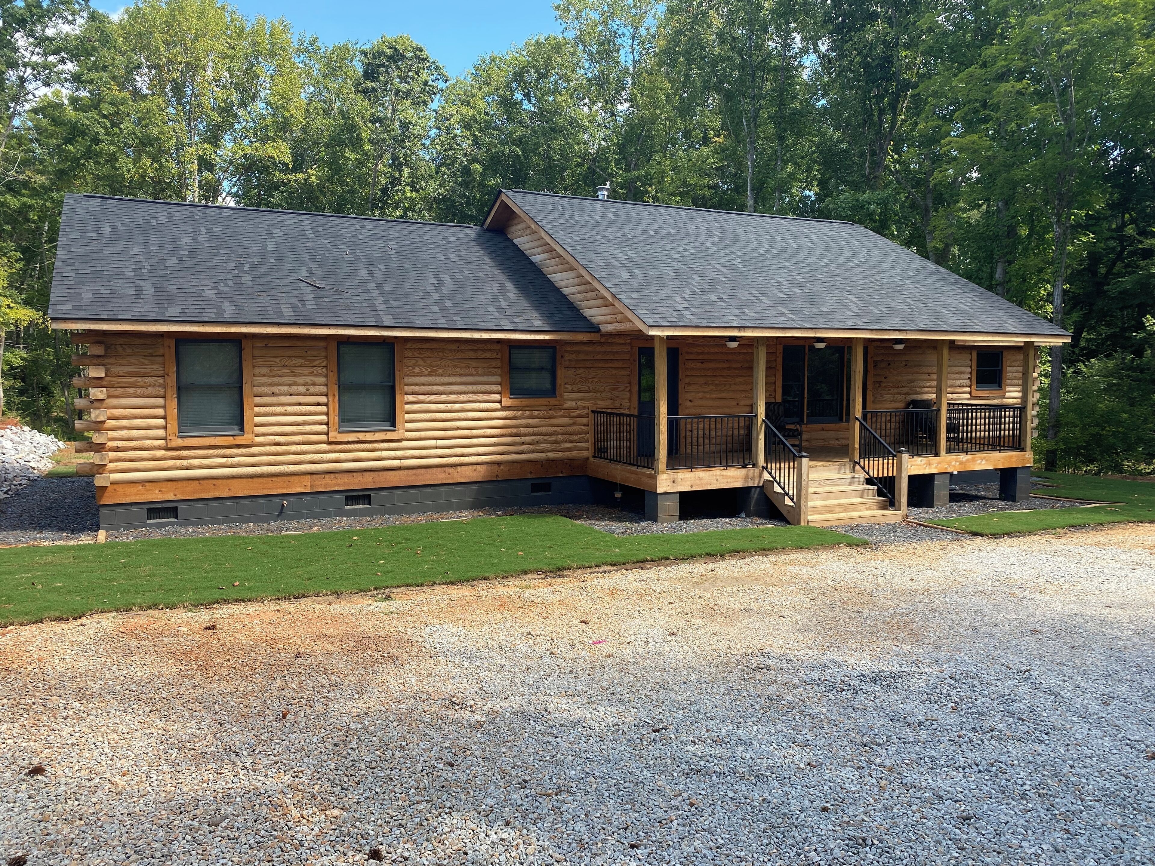 A log cabin with a porch, a covered deck, and a gravel driveway.