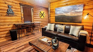 Ein gemütliches Blockhaus-Interieur mit Esstisch aus Holz, Ledersofa und einem Landschaftsbild.
