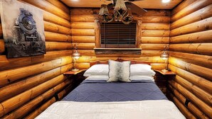 Ein schlicht eingerichtetes Schlafzimmer im Chalet-Stil mit einem Bett, zwei Nachttischen, einem Fenster mit Jalousien und einer Wandlampe.