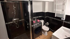 Et moderne badeværelse med en bruseniche, toilet, vaskemaskine og håndvask.