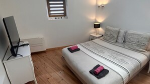 Et soveværelse med seng, skrivebord, lille vindue og vægmonteret lampe.