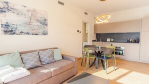 Een moderne woonkamer met een bank, een eettafel en stoelen. Er is een keuken met een fornuis, magnetron en kastjes.