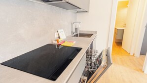 Et moderne køkken med en sort induktionskogetop, en integreret opvaskemaskine og en stålvask.