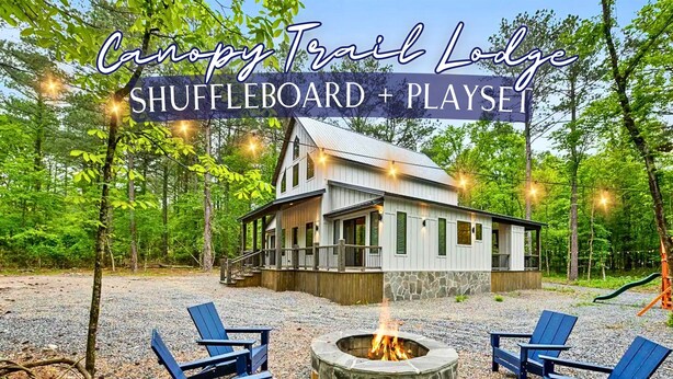 En hytte med shuffleboard og legeplads, omgivet af træer og et bålsted.