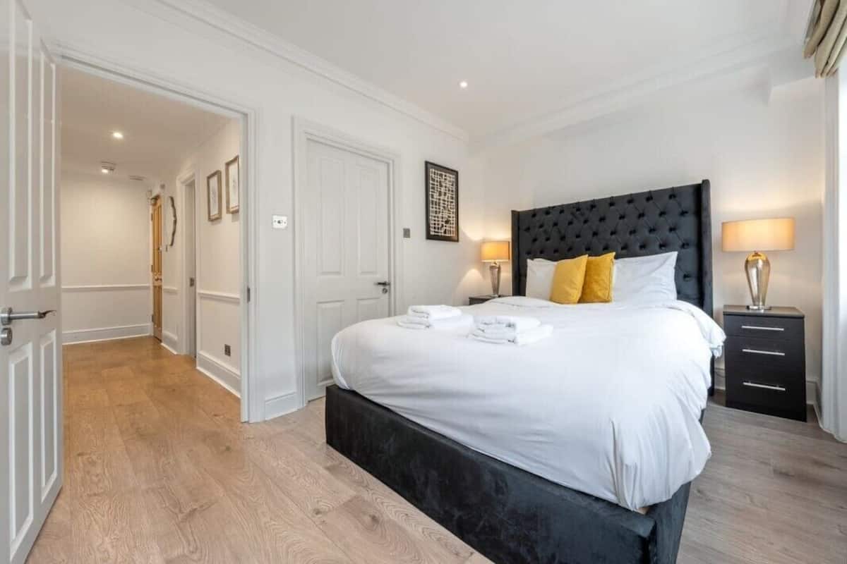 A hotel room with a large bed, white linens, a dark headboard, two bedside lamps, and a small bedside table.