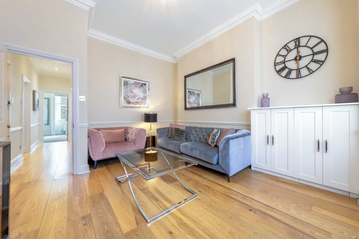 A living room with a glass coffee table, two sofas, a cabinet, and a wall clock.