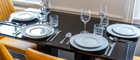 Una mesa de comedor dispuesta con platos, cubiertos y vasos, rodeada de sillas amarillas.