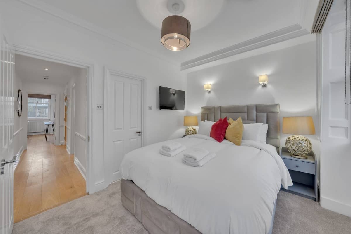 A hotel bedroom with a large bed, bedside lamps, a flat-screen TV, and a view of the hallway.
