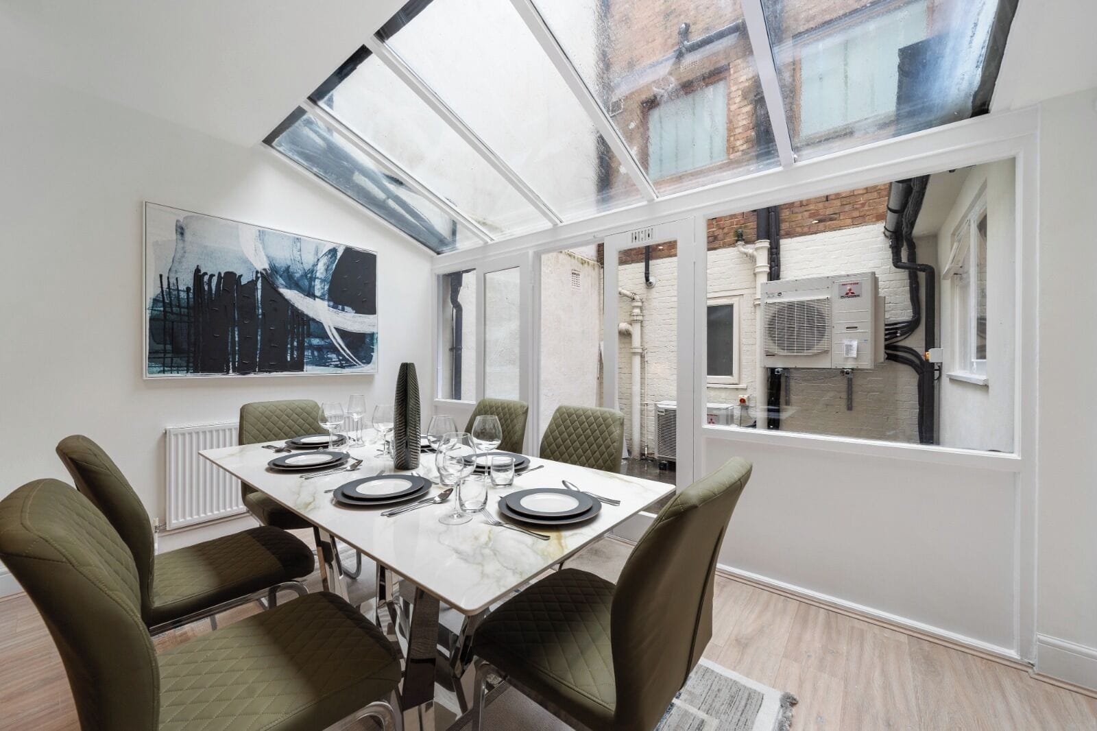 Un comedor con una mesa preparada para seis personas, ventanas amplias y vista a la calle.