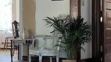 Une pièce avec un plancher en bois, une chaise blanche, une table avec un plateau en verre et une grande plante en pot.