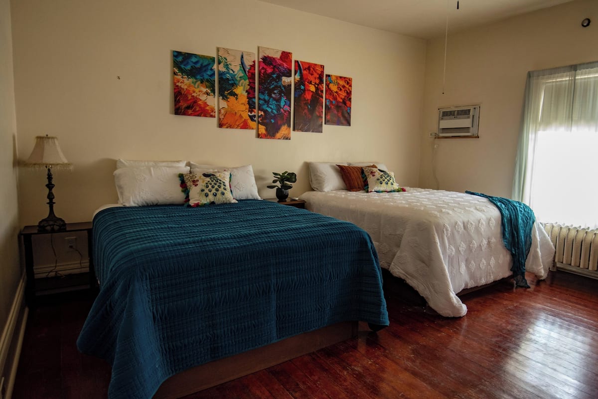 A bedroom with two beds, a nightstand, a lamp, and a radiator.